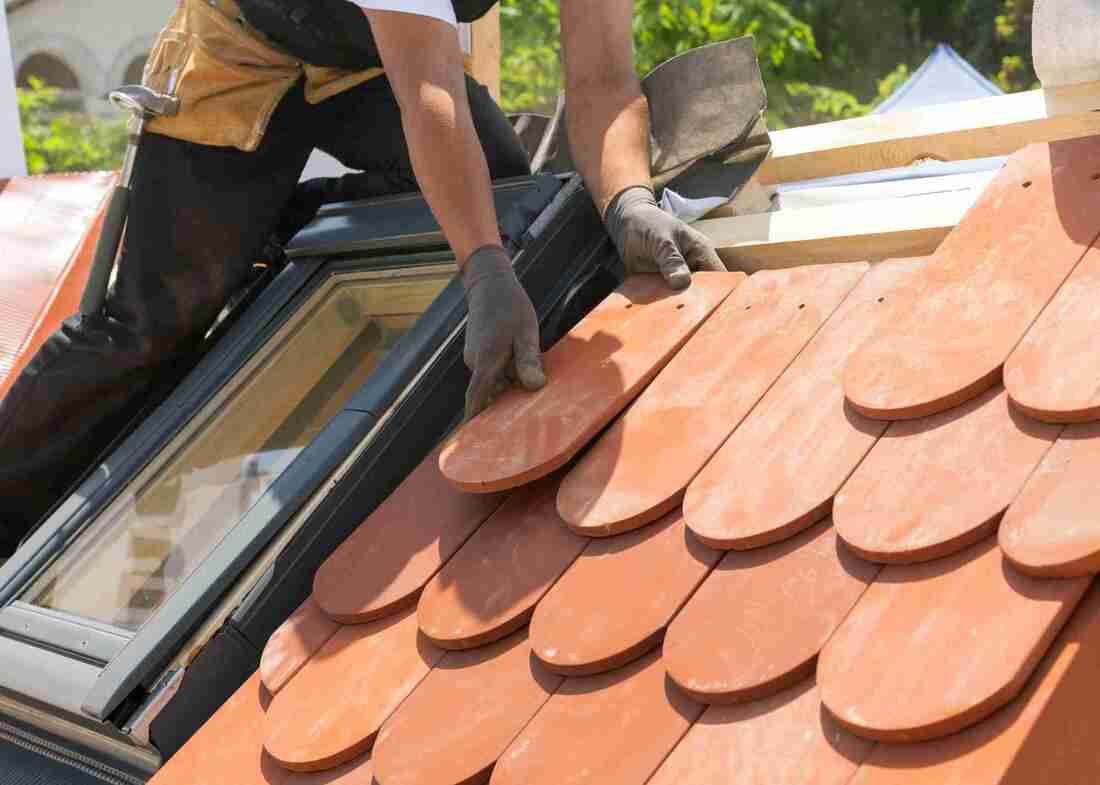 Roofer installing red tiles on roof